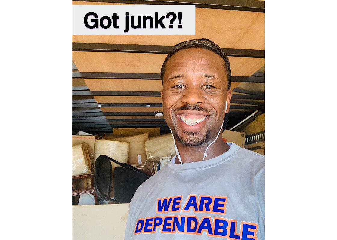 Dallas Junk Removal Expert A smiling Dallas junk removal expert in a "We Are Dependable" shirt standing in front of a loaded truck with "Got junk?!" text.