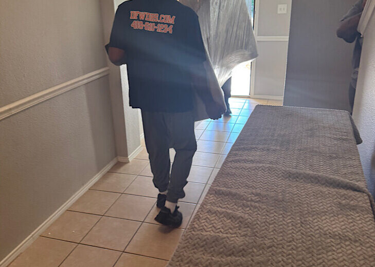 mover-carrying-wrapped-furniture-into-house A professional mover carrying plastic-wrapped furniture through a hallway into a home